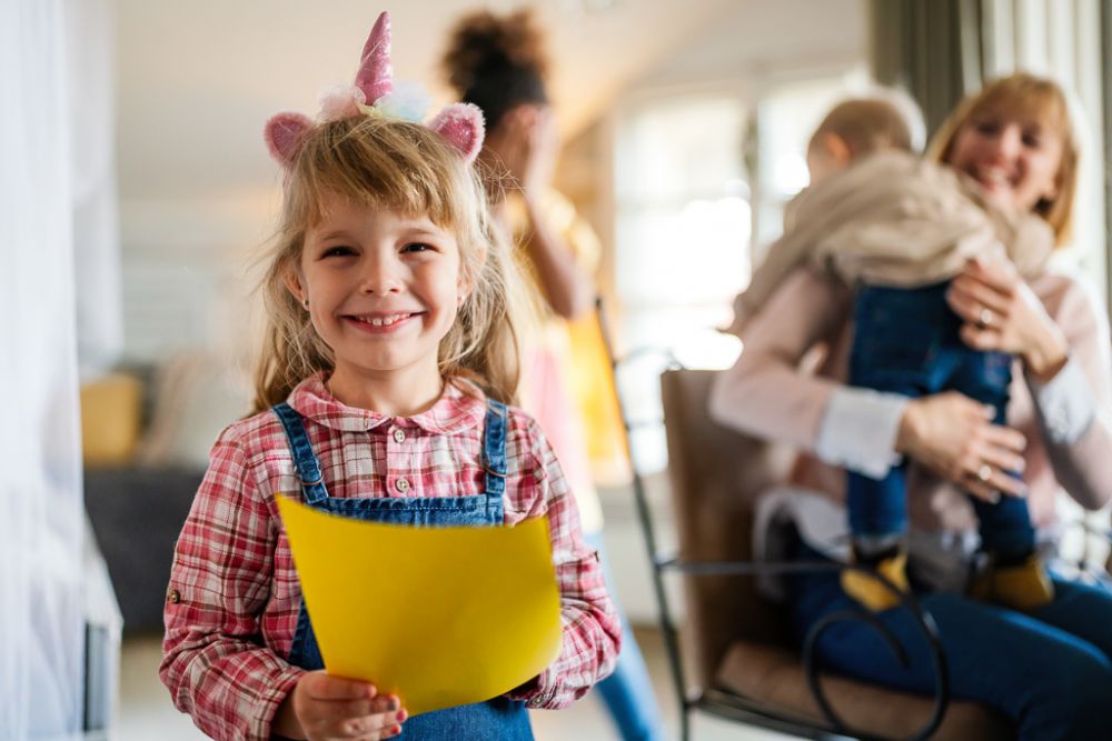 Portrait of a happy cute little girl smiling while her single mother with siblings playing on a background